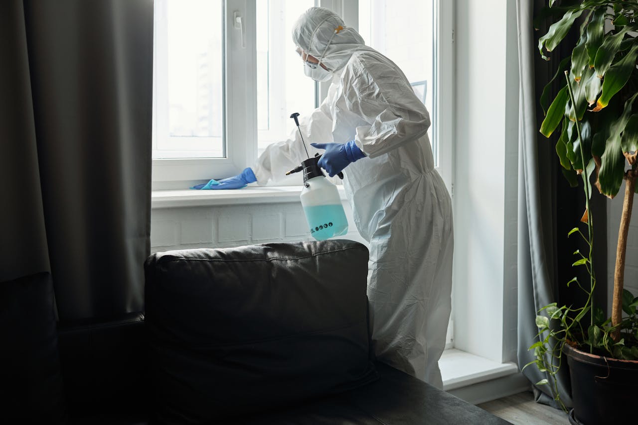 hero-img Person in PPE disinfecting indoor window area during COVID-19 pandemic.